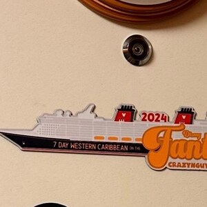 May include: A white and black cruise ship magnet with the word "Fantasy" in orange script. The magnet also includes the text "7 Day Western Caribbean" and "2024". The background is a light beige color.