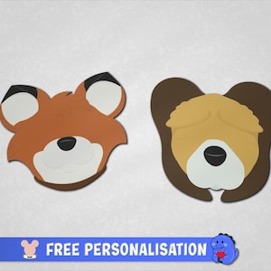 May include: Two flat animal-shaped cutouts featuring a fox head with orange, white, and black details, and a dog head with tan and dark brown colours. A blue banner at the bottom displays the text "FREE PERSONALISATION" with a small icon.