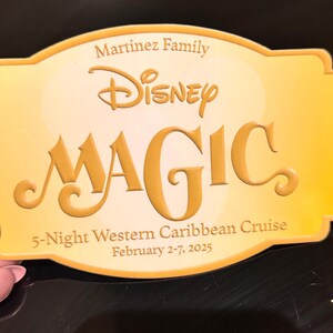 May include: A golden-yellow Disney Magic cruise card with the Martinez Family name. The card features the Disney logo and the word "MAGIC" in large, embossed letters. It also states "5-Night Western Caribbean Cruise, February 2-7, 2025."