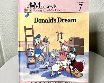 May include: A pink and white book with the title "Mickey's Young Readers Library: Donald's Dream" and a picture of Donald Duck and his family. The book is volume 7 of the series.