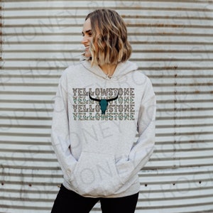 May include: A gray hoodie with a teal and black bull skull graphic and the text "Yellowstone" repeated four times.