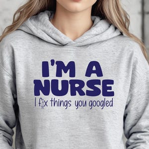 May include: A light gray hooded sweatshirt with a front pocket. The sweatshirt features the text "I'M A NURSE" in dark blue block letters, with the phrase "I fix things you googled" below it.