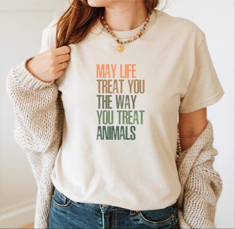May include: A beige t-shirt with a message that reads "May life treat you the way you treat animals". The text is in a rainbow gradient.