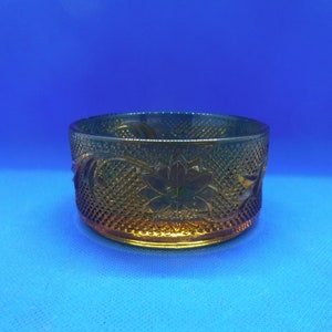 May include: A vintage amber-colored glass bowl with a floral and diamond pattern. The bowl has a round shape and is likely used for serving or display. The intricate design adds a touch of elegance to the piece.