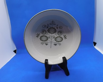 May include: A white ceramic bowl with a gray floral design. The bowl is on a black stand against a blue background.
