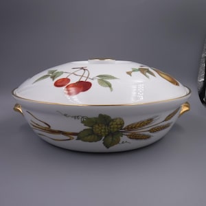 May include: White oval serving dish with a lid, featuring a gold rim and handles. The dish is decorated with illustrations of cherries, wheat, and hops. A gold accent is on the lid.