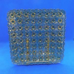 May include: A square glass plate with a scalloped edge and a repeating pattern of gold stars and circles.