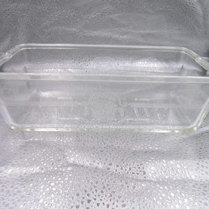 Könnte beinhalten: Eine transparente Glas-Kastenform mit einem dekorativen Design auf dem Boden. Die Form ist leer und hat eine rechteckige Form.