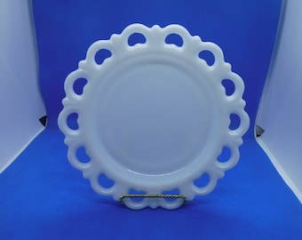 May include: A white milk glass plate with a scalloped edge and openwork design. The plate is on a blue background.