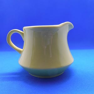 May include: A light green ceramic creamer with a rounded body and a curved handle.