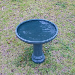 May include: A dark teal bird bath with a round basin and a pedestal base. The basin is filled with water. The bird bath is set on green grass. The bird bath is approximately 60 cm in height.