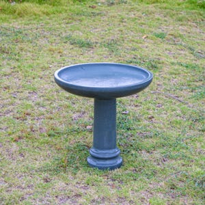 May include: A dark teal bird bath with a round basin and a pedestal base. The bird bath is made of a solid material and is placed on a grassy lawn. The bird bath is designed to provide water for birds.