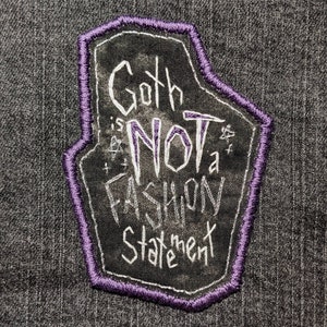 May include: A purple embroidered patch with a black background and white text that reads "Goth is Not a Fashion Statement".