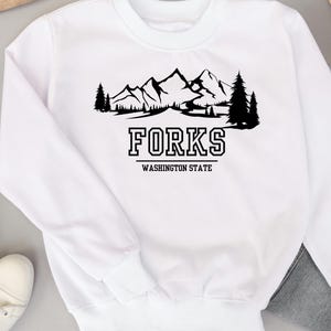 May include: White sweatshirt with a black graphic of a mountain range and trees with the text "FORKS WASHINGTON STATE" underneath.