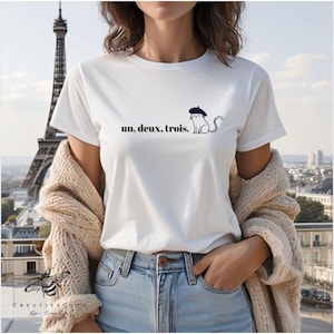 May include: White t-shirt with a black cat wearing a beret and the text "un. deux. trois."
