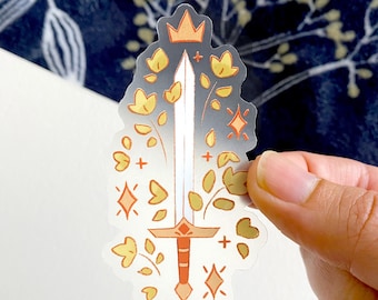 May include: A clear sticker featuring a sword design with a crown, flowers, and stars. The sword has a white blade and a red hilt. Yellow flowers and orange stars surround the sword, with a gradient gray background.