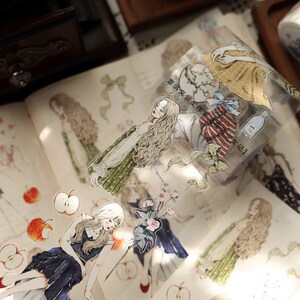 May include: Decorative stickers featuring illustrations of women in vintage dresses, apples, and floral elements. The stickers are on a clear backing, with some text visible. The overall aesthetic is soft and whimsical.
