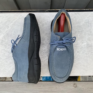 May include: A pair of blue suede lace-up shoes with black soles. The shoes have the word "KANI" embroidered on the front.