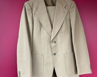 May include: A beige suit jacket with two patch pockets and three buttons. The jacket has a notch lapel and is made of a textured fabric.
