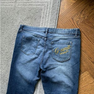 May include: Blue denim jeans with a gold embroidered logo that says "G-Unit Clothing Co."