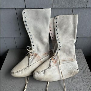 May include: A pair of off-white leather boots with laces and eyelets. The boots are tall and have a pointed toe.