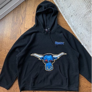 May include: Black fleece hoodie featuring a blue bull's head graphic and the text "The Rock" in blue and white lettering.