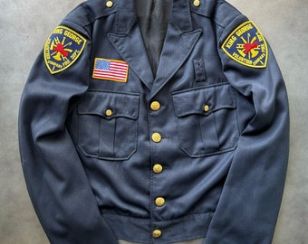 May include: A dark blue jacket with gold buttons and two pockets. The jacket has a patch on the left side that says "King George Volunteer Fire Dept. Company 1" and a small American flag patch on the right side. The jacket also has a patch on the right side that says "King George Volunteer Fire Dept. Company 1".