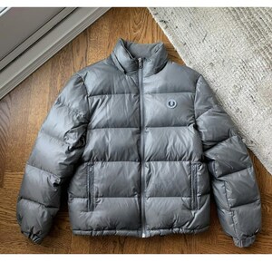 May include: A grey puffer jacket with a zip fastening and a small logo on the chest.
