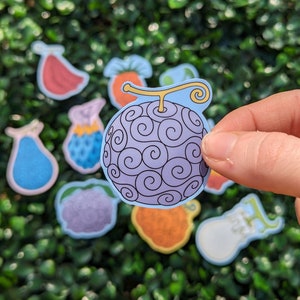 Puede incluir: Un conjunto de pegatinas de frutas coloridas que incluyen una fruta de espiral p&uacute;rpura y azul, una fruta roja, una fruta azul en forma de pera, una fruta p&uacute;rpura, una fruta amarilla y naranja, una fruta blanca y una fruta naranja.