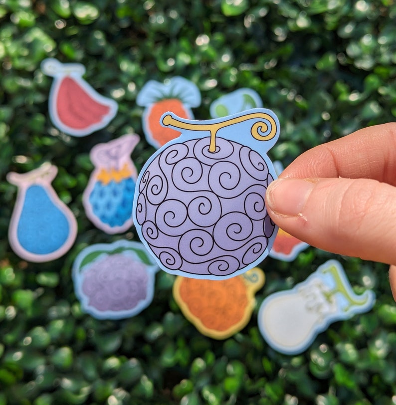 Puede incluir: Un conjunto de pegatinas de frutas coloridas que incluyen una fruta de espiral p&uacute;rpura y azul, una fruta roja, una fruta azul en forma de pera, una fruta p&uacute;rpura, una fruta amarilla y naranja, una fruta blanca y una fruta naranja.