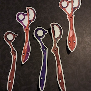 May include: Five decorative scissors with intricate designs. The scissors are in various colors, including red, pink, purple, and white. The scissors are cut out of paper and have a glossy finish.