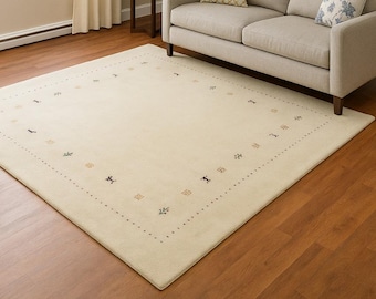 Alfombra Gabbeh minimalista color crema: alfombra de lana anudada a mano con motivos tribales de animales y árboles. Alfombra moderna de estilo persa con decoración suave y neutra.