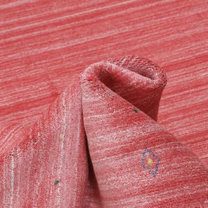 Puede incluir: Una alfombra roja con un patr&oacute;n de rayas horizontales texturizadas en varios tonos de rojo y blanco. La superficie presenta peque&ntilde;os motivos geom&eacute;tricos bordados dispersos en verde, azul y amarillo, incluyendo formas de zigzag y diamantes.