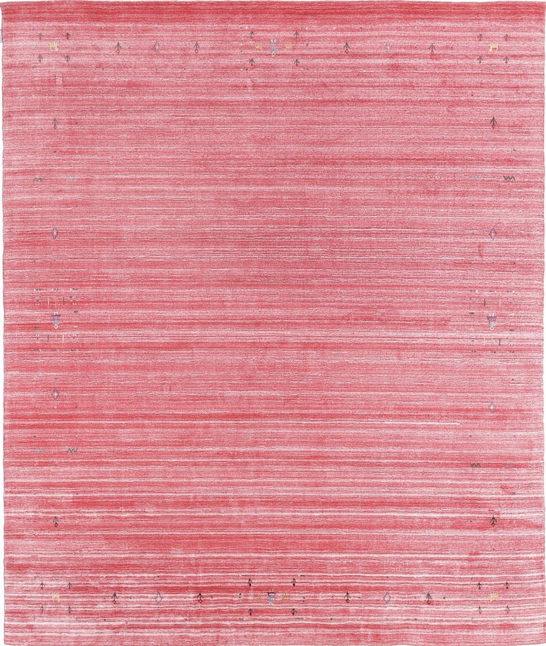 Puede incluir: Una alfombra rectangular con una base de color rojo vibrante y estr&iacute;as horizontales blancas en toda la superficie. El borde est&aacute; definido por una serie de peque&ntilde;os motivos geom&eacute;tricos espaciados en tonos apagados de azul, amarillo y marr&oacute;n oscuro.