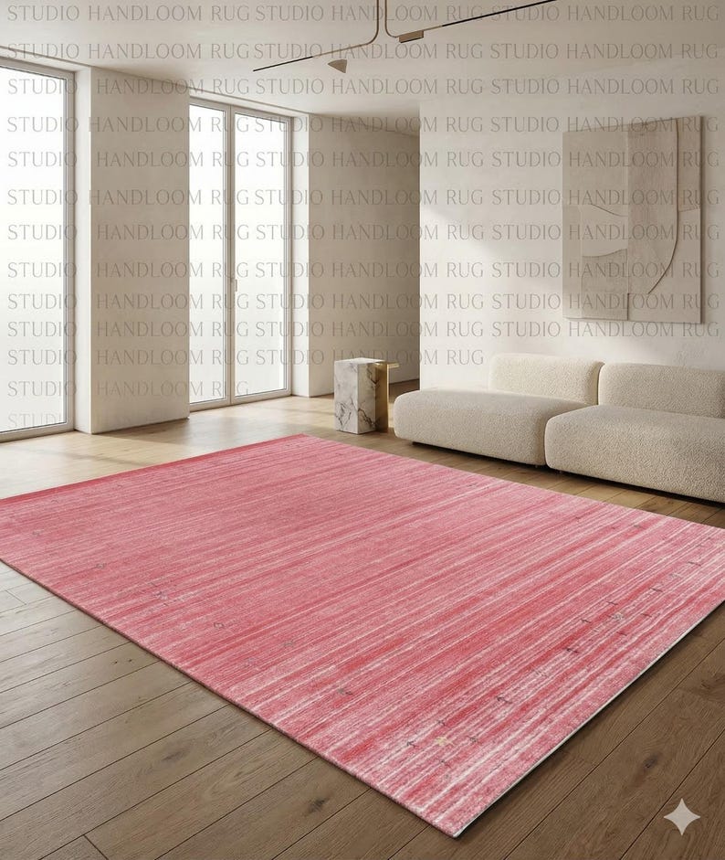 Puede incluir: Una alfombra rectangular que presenta una paleta de colores rosa vibrante con sutiles estr&iacute;as horizontales blancas y una textura desgastada en toda la superficie. La alfombra est&aacute; colocada sobre un suelo de madera en una habitaci&oacute;n clara.