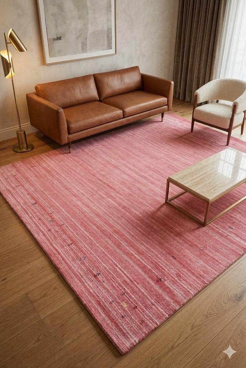 Puede incluir: Una alfombra rectangular grande en tonos rosa y blanco, con un patr&oacute;n lineal. La alfombra est&aacute; colocada en un sal&oacute;n, junto a un sof&aacute; de cuero marr&oacute;n, un sill&oacute;n blanco y una mesa de centro con tapa de m&aacute;rmol.