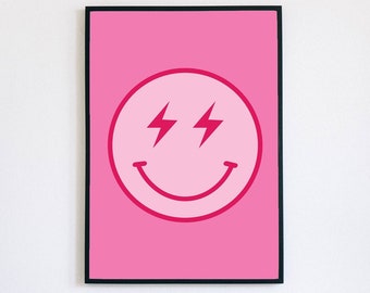 May include: A framed pink wall art print featuring a smiling face with lightning bolt eyes. The artwork has a light pink background with a darker pink smiley face design. The frame is black.
