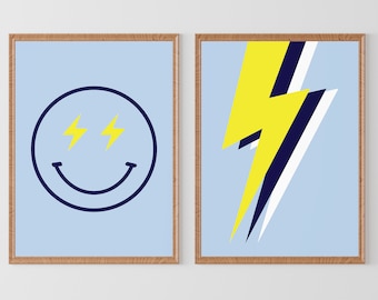May include: Two framed prints on a light blue background. The print on the left features a yellow smiley face with lightning bolt eyes. The print on the right features a yellow lightning bolt with black and white accents.