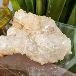 May include: A cluster of clear quartz crystals with a milky white hue. The crystals are clustered together in a rough, natural formation.