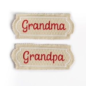 May include: Two embroidered patches with the words "Grandma" and "Grandpa" in red script. The patches have a beige background with a quilted pattern and a white border. The edges are scalloped.