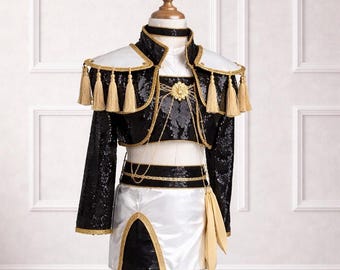 May include: A black sequined crop top and skirt set with gold trim and accents. The outfit includes a white and gold bolero with gold tassels and a matching choker. The skirt is white with a black panel and gold trim. The outfit is displayed on a mannequin.