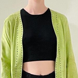 Peut inclure: Une veste ouverte vert citron à manches longues, ornée d'une rangée verticale de petites découpes circulaires régulièrement espacées le long de la patte de boutonnage avant et des poignets, portée sur un haut court noir et un pantalon noir.