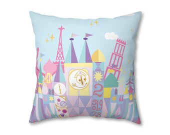 May include: A pastel-colored pillow featuring a whimsical illustration of a fairytale castle with a clock face and the numbers 2, 5, 1, 9, 7, and 8. The castle is surrounded by smaller buildings and trees, all in pastel colors.