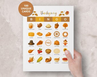 May include: Thanksgiving Bingo game card with colorful illustrations of fall-themed items like turkey, pumpkin pie, and cornucopia. The card has the text "Thanksgiving" and "100 UNIQUE CARDS". The card is held by a hand.