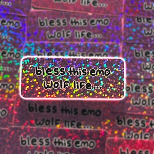 May include: A rectangular sticker with the text "bless this emo wolf life..." in a handwritten style. The sticker has a holographic, glittery design with a pink border and background. Other stickers with the same text are visible.