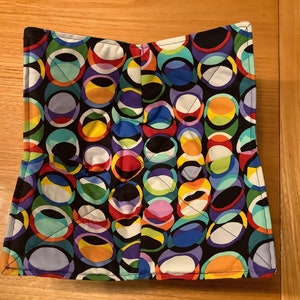 May include: A colourful pot holder with a black background and a pattern of overlapping circles in various shades of blue, green, red, yellow, and purple.