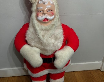May include: A vintage Santa Claus doll with a red suit, hat, and white faux fur trim. The doll has a painted face with a white beard and mustache, black boots, and white gloves. The doll is standing upright.
