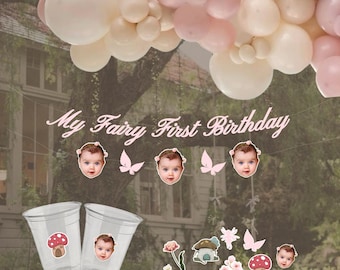 May include: A pink and white balloon arch with a banner that says "My Fairy First Birthday". There are also several small stickers with fairy-themed images, including butterflies, flowers, and mushrooms.