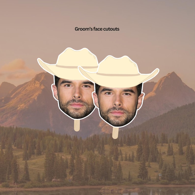 May include: Two cardboard cutouts of a man's face wearing a tan cowboy hat. The cutouts are on sticks and are in front of a mountain landscape.