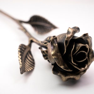 Bronze stained metal rose lays on the white surface. The metal flower is 12 inches long.